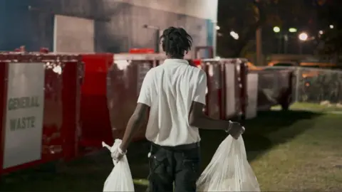 Courtesy of Close the Loop Caribbean A man carries two bags of rubbish to rubbish bins